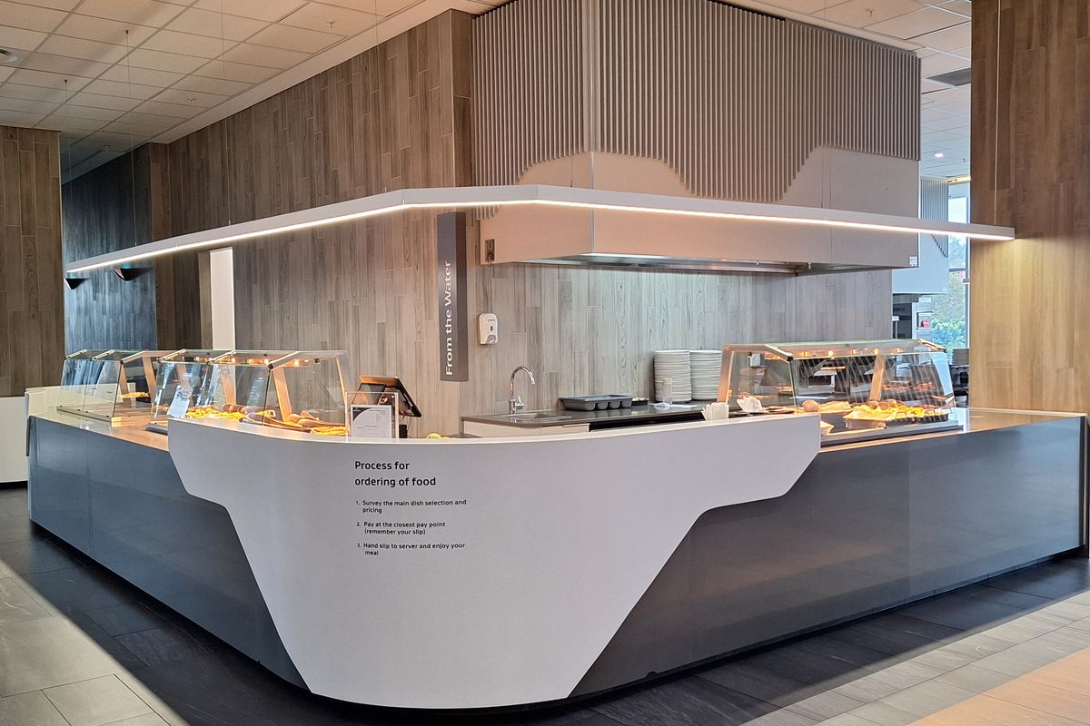 Modern commercial food service station featuring a sleek, custom-built counter, integrated sink, professional extractor hood, and contemporary wood-look finishes.