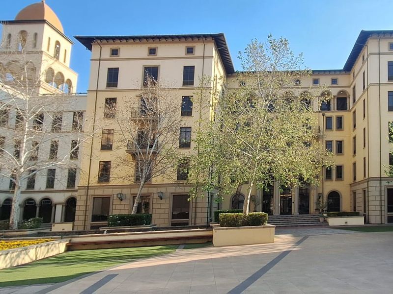 A view of the multi-story office building facade featuring classic architectural details, arched windows, and a well-maintained paved courtyard entrance.