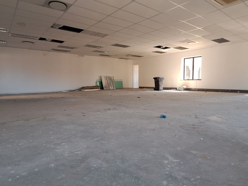 A large, open-plan office space featuring a suspended ceiling with missing tiles and unfinished concrete flooring, ready for renovation or fit-out.
