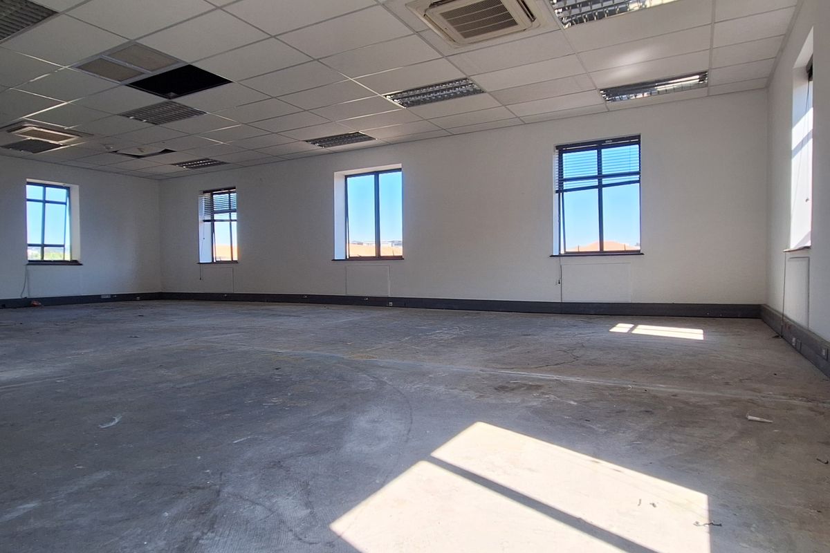 A large, open-plan office space featuring a suspended ceiling, perimeter trunking, and multiple windows, currently in need of flooring and ceiling repairs.