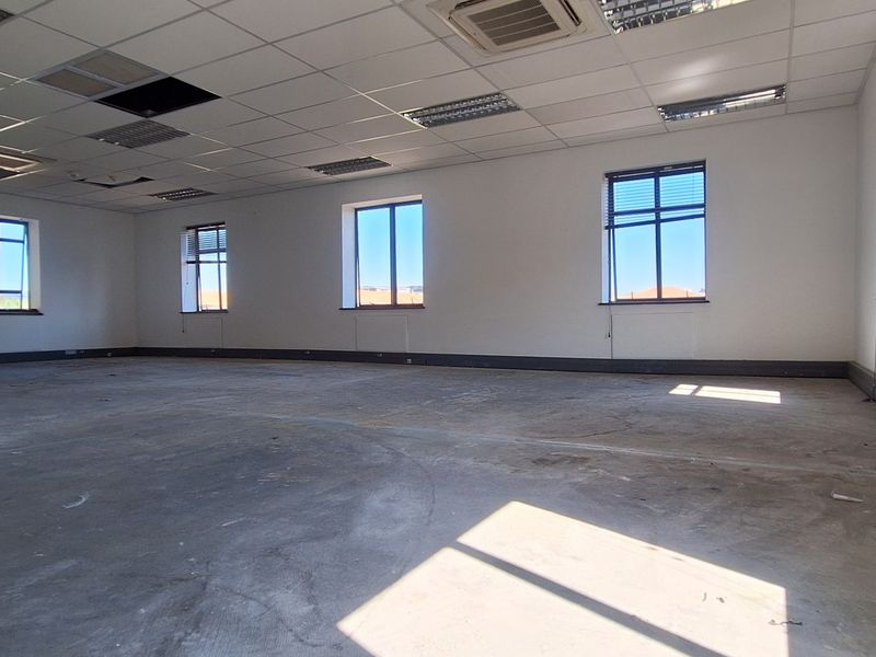 A large, open-plan office space featuring a suspended ceiling, perimeter trunking, and multiple windows, currently in need of flooring and ceiling repairs.