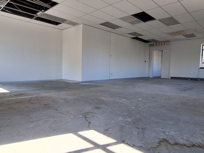 An empty, open-plan office space featuring a suspended ceiling with missing tiles and an exposed concrete floor, requiring renovation and finishing.