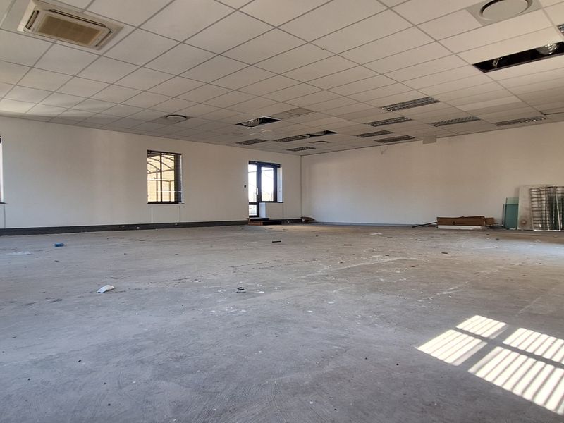 A large, open-plan office space featuring a suspended ceiling with recessed lighting and air conditioning, currently in need of flooring and ceiling repairs.