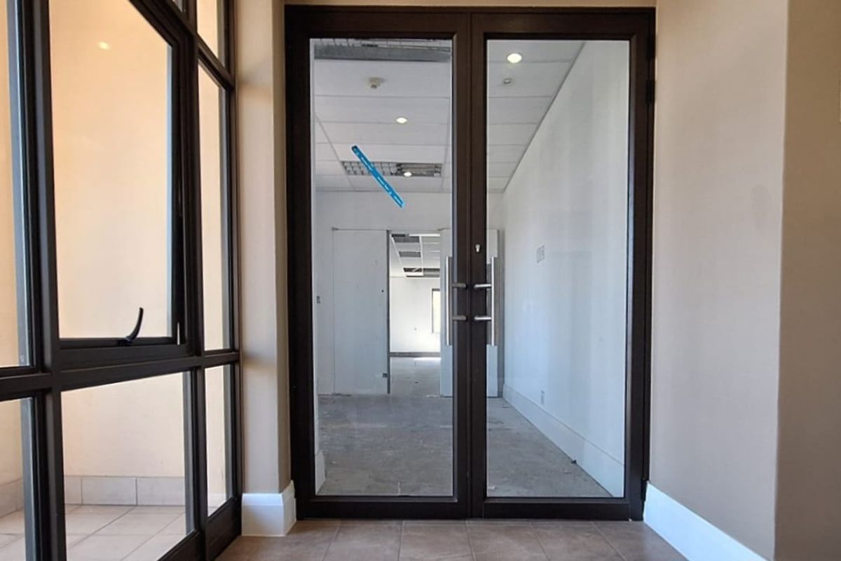 Entrance area featuring double glass doors, tiled flooring, and recessed lighting, leading into an open-plan office space with suspended ceiling tiles.
