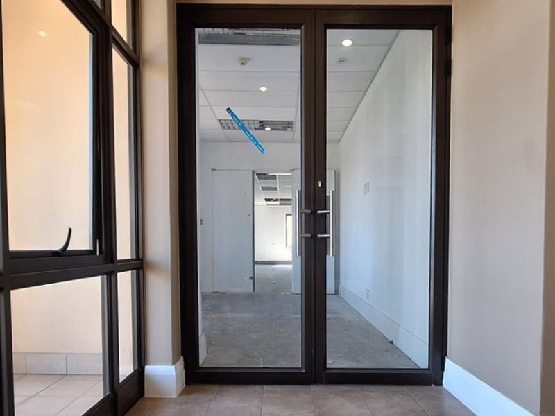 Entrance area featuring double glass doors, tiled flooring, and recessed lighting, leading into an open-plan office space with suspended ceiling tiles.