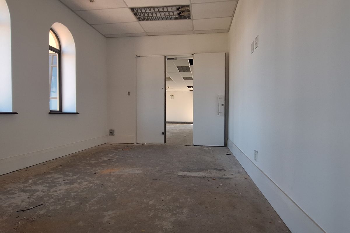 An empty office space featuring arched windows, a suspended ceiling, and unfinished concrete flooring, ready for renovation or fit-out.
