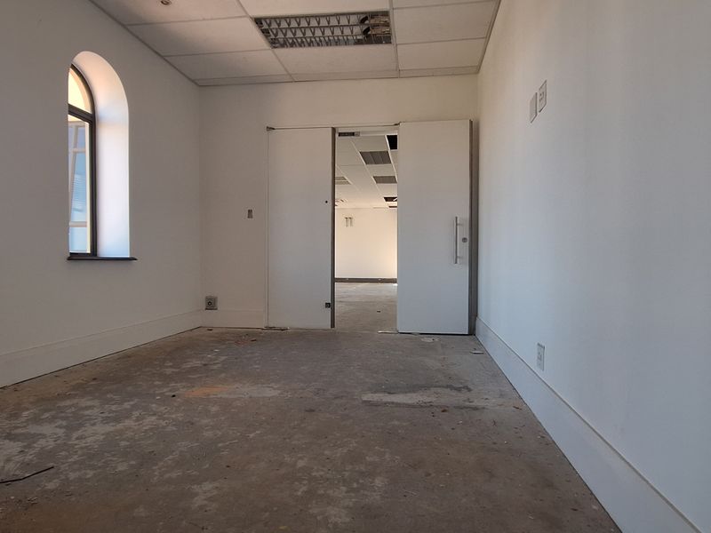 An empty office space featuring arched windows, a suspended ceiling, and unfinished concrete flooring, ready for renovation or fit-out.