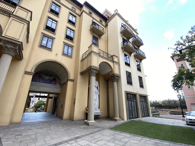 A multi-story office building facade featuring classical architectural elements, arched entryways, balconies, and stone-paved ground level access.