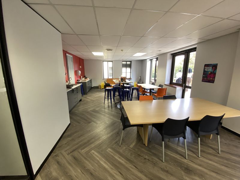 Spacious open-plan office area featuring a functional kitchenette, herringbone vinyl flooring, and a suspended ceiling with recessed lighting, suitable for collaborative work.