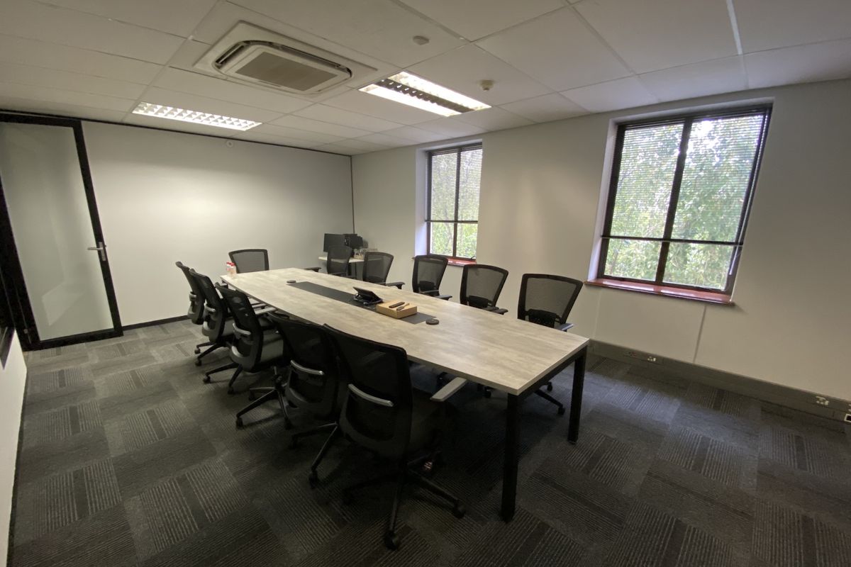 A professional office boardroom featuring carpeted flooring, suspended ceilings with integrated lighting, central air conditioning, and large windows providing natural light.