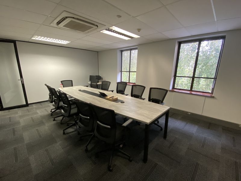 A professional office boardroom featuring carpeted flooring, suspended ceilings with integrated lighting, central air conditioning, and large windows providing natural light.