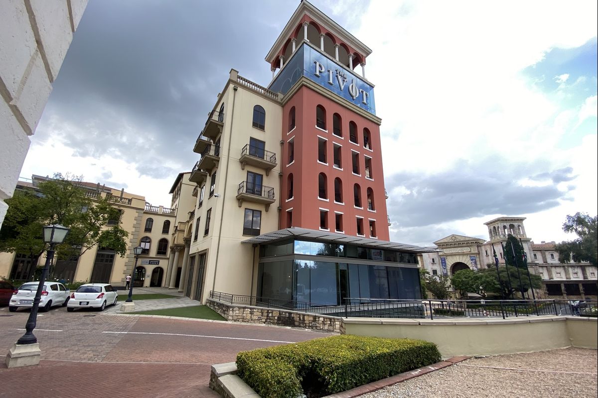 Exterior view of The Pivot office building featuring a multi-story facade, decorative tower, balconies, and a modern glass-enclosed ground floor extension.