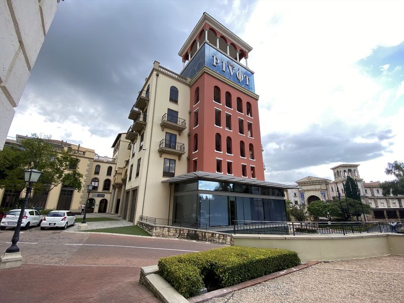 Exterior view of The Pivot office building featuring a multi-story facade, decorative tower, balconies, and a modern glass-enclosed ground floor extension.