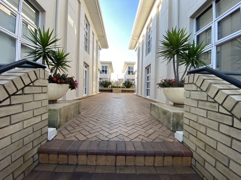 A paved walkway between two office building wings, featuring brick retaining walls and well-maintained exterior finishes.