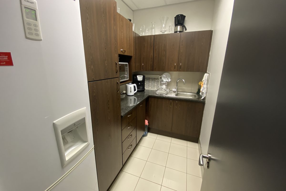 A compact office kitchenette featuring dark wood-finish cabinetry, granite countertops, a stainless steel sink, and tiled flooring.