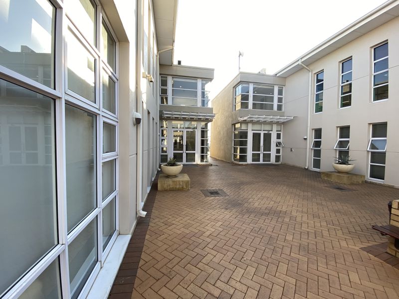 A well-maintained paved courtyard area between office building wings, featuring large glass windows and modern architectural finishes.