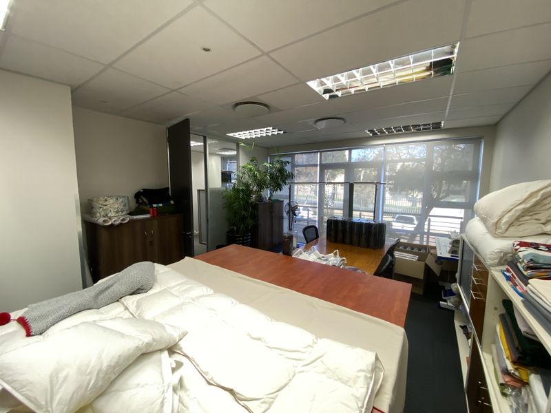 A functional office space featuring a suspended ceiling with recessed lighting, large windows with roller blinds, and a glass partition for added privacy.