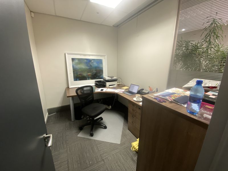 A compact private office space featuring carpeted flooring, a suspended ceiling with recessed lighting, and an internal glass partition wall.