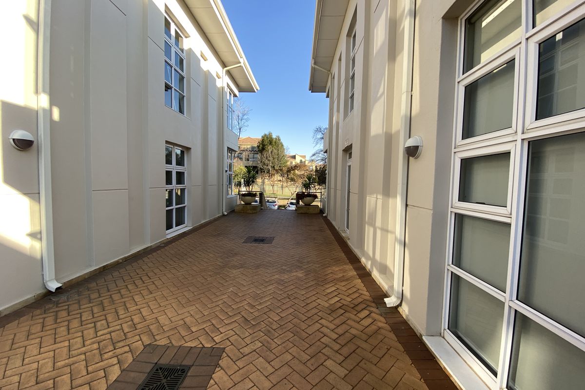 A paved exterior walkway situated between two office building wings, featuring modern multi-pane windows and wall-mounted exterior lighting.