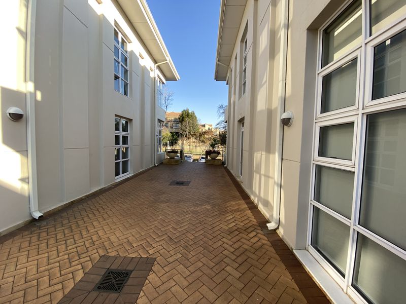 A paved exterior walkway situated between two office building wings, featuring modern multi-pane windows and wall-mounted exterior lighting.
