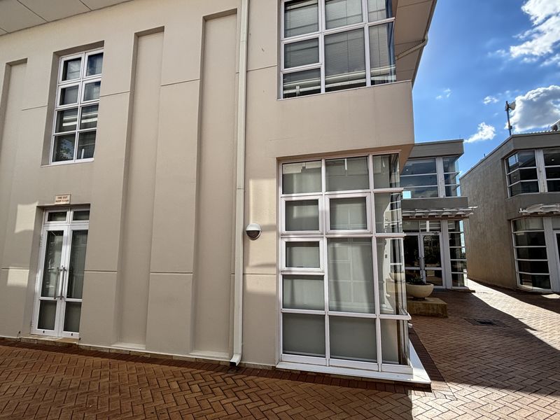 A modern office building exterior featuring a paved courtyard, multi-level facade, and large glass windows.