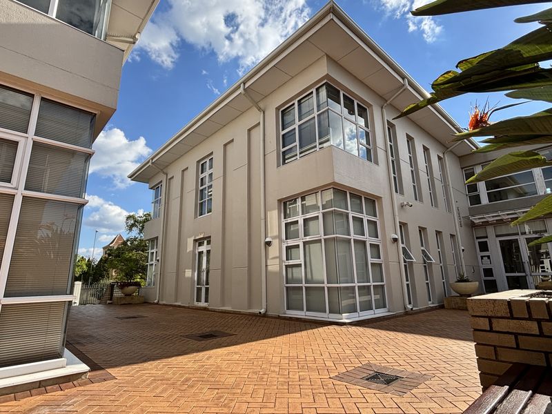 A well-maintained exterior courtyard area featuring paved flooring and modern multi-story office building facades with large windows.