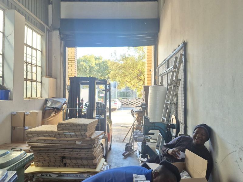 Industrial warehouse space featuring high ceilings, large steel-framed windows, and a wide roller shutter door for vehicle or equipment access.