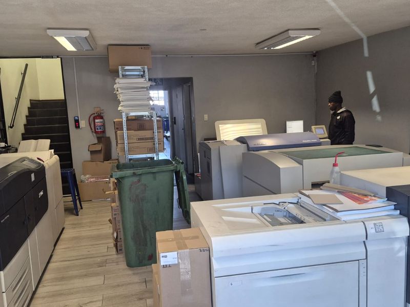 Industrial utility space currently utilized as a printing facility, featuring tiled flooring, overhead lighting, and wall-mounted air conditioning unit.