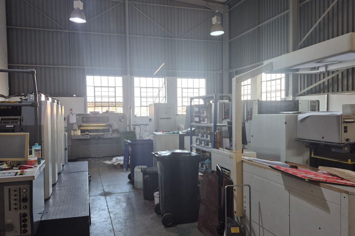 Industrial workshop space featuring high-bay lighting, concrete flooring, and large multi-pane windows, currently utilized for printing operations.