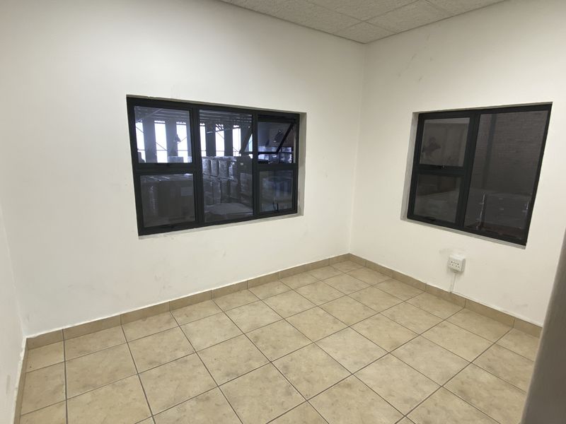 A vacant office space featuring tiled flooring, drop ceiling, and aluminium-framed windows, suitable for a professional workspace.