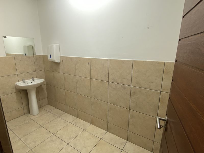 A clean, functional bathroom featuring a pedestal basin, tiled flooring, and half-tiled walls, providing a simple and practical utility space.