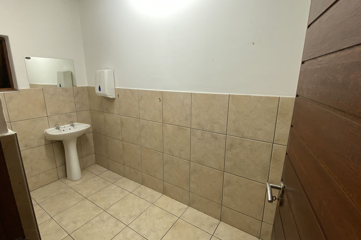 A clean, functional bathroom featuring a pedestal basin, tiled flooring, and half-tiled walls, providing a simple and practical utility space.
