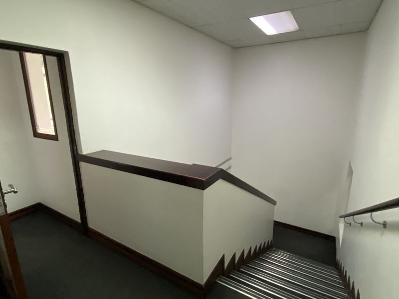 A functional industrial hallway featuring a staircase with a handrail, drop ceiling with recessed lighting, and neutral wall finishes.