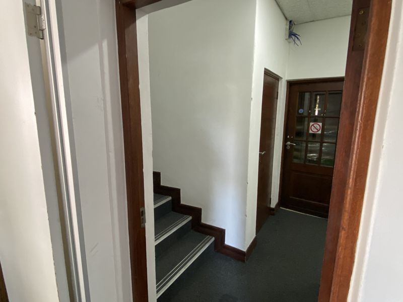 A functional industrial hallway featuring a staircase, timber door frames, and carpeted flooring, providing access to multiple internal areas.