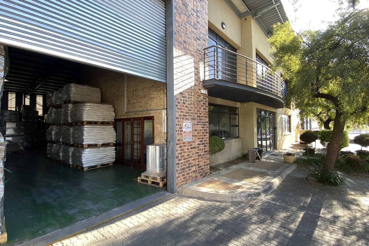Industrial warehouse exterior featuring a large roller shutter door, brick facade, and an upper-level balcony with metal railings.
