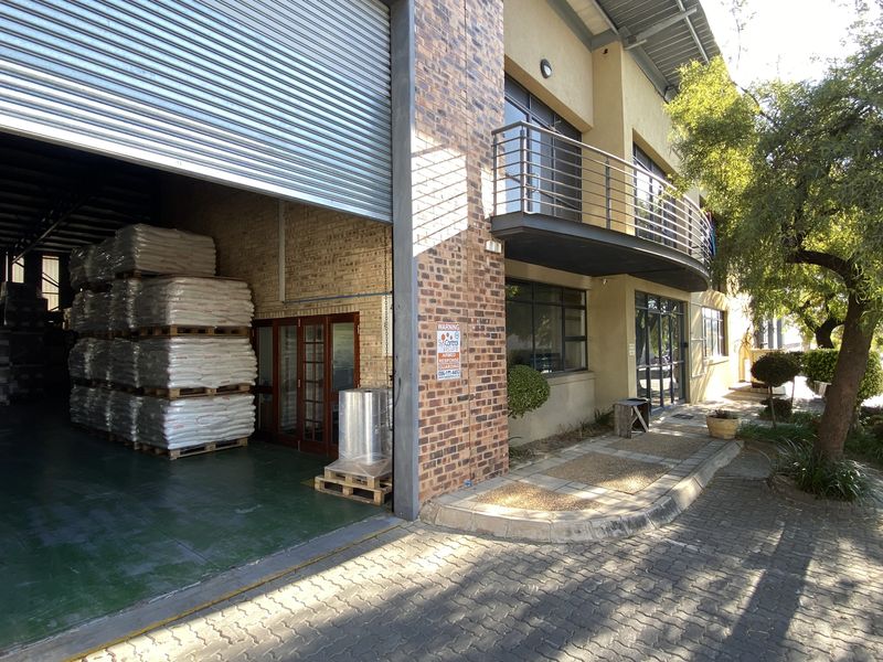 Industrial warehouse exterior featuring a large roller shutter door, brick facade, and an upper-level balcony with metal railings.