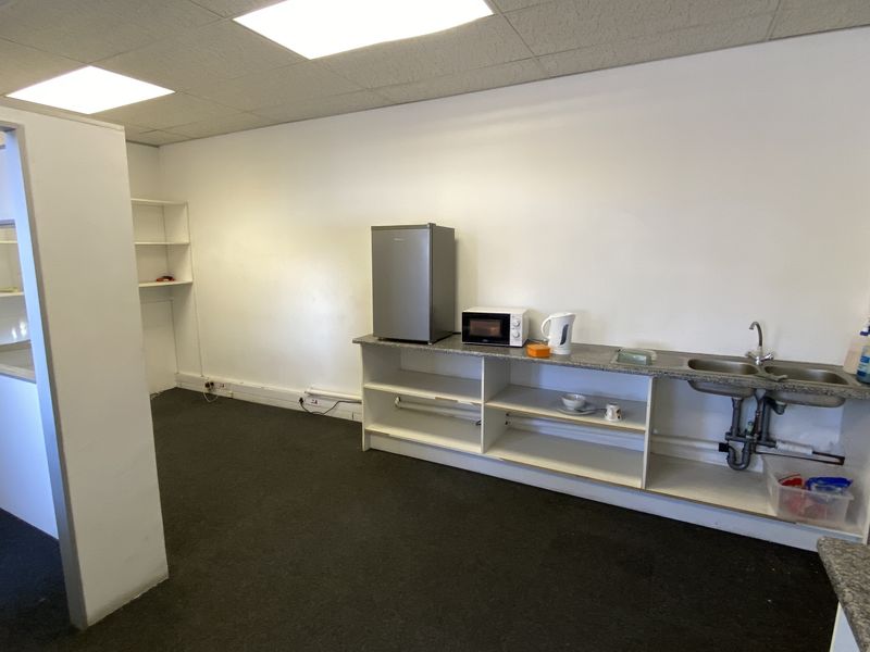 A functional industrial kitchenette area featuring a stainless steel double sink, laminate countertop, and open built-in shelving within a partitioned office space.