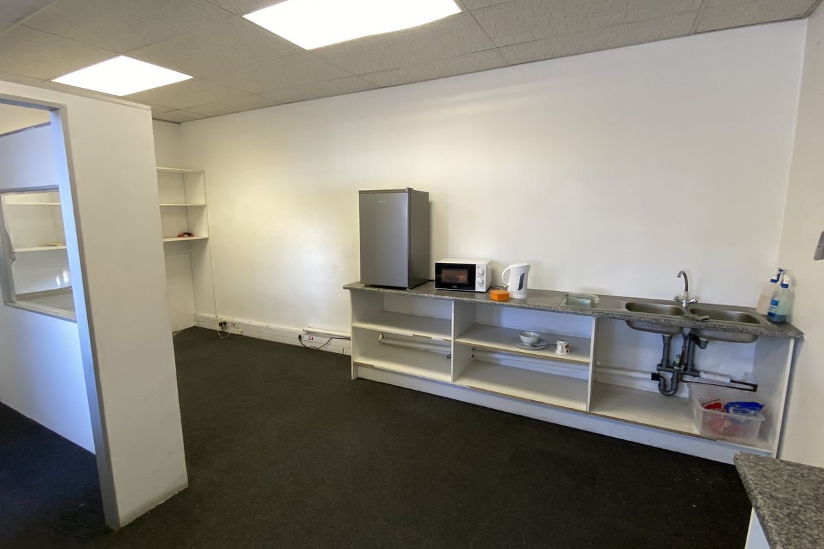 A functional industrial kitchenette area featuring a stainless steel double sink, laminate countertop, and open built-in shelving within a partitioned office space.