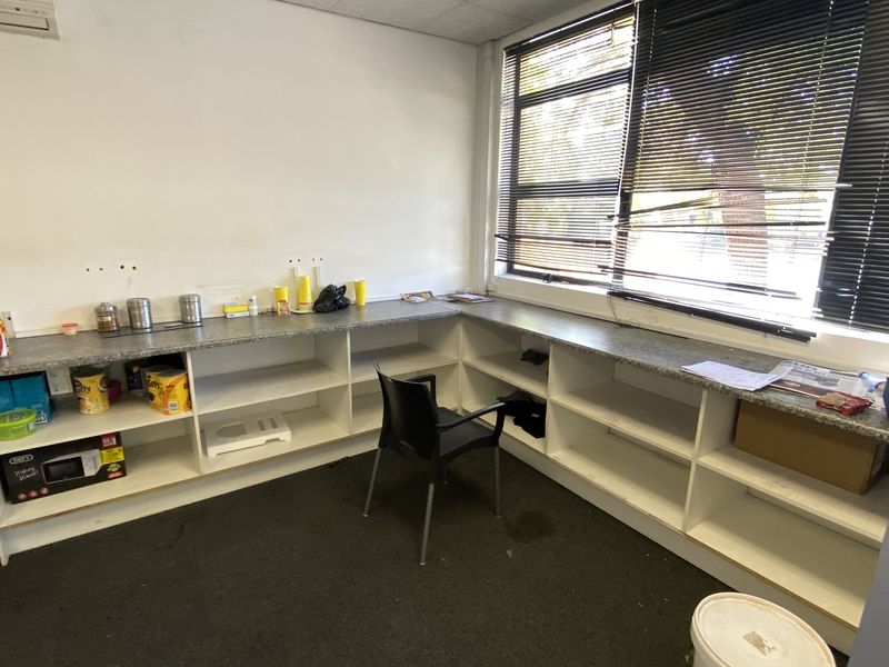 An industrial office space featuring built-in L-shaped shelving with laminate countertops, venetian blinds, and an air conditioning unit.