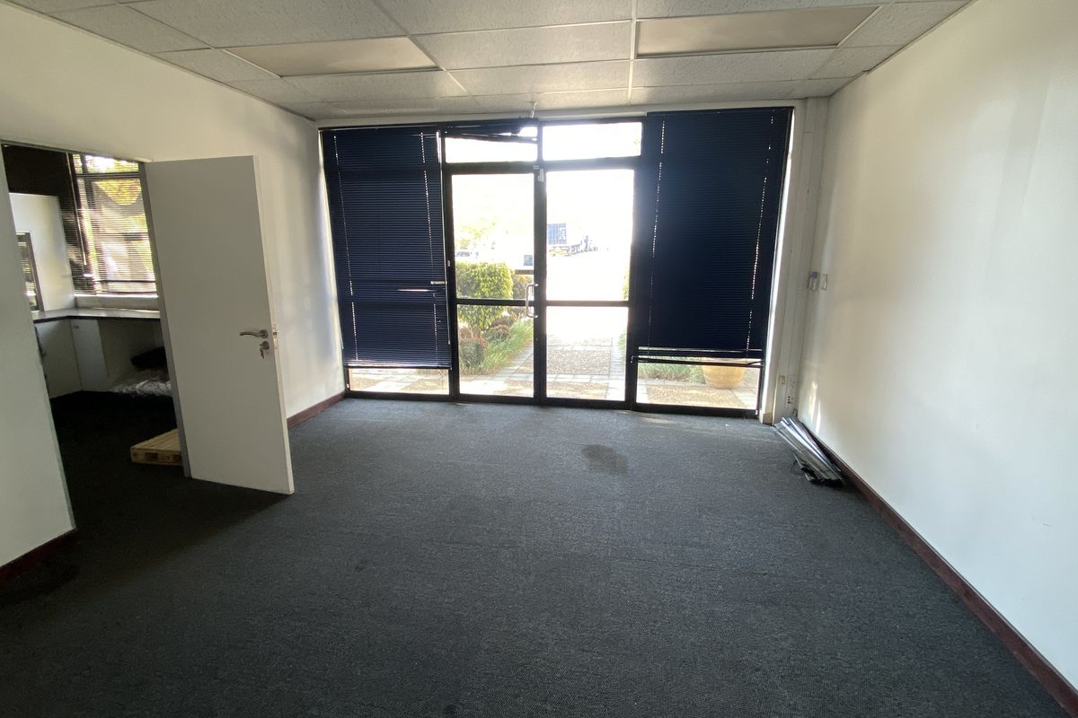An empty office space featuring carpeted flooring, a suspended ceiling, and a glass entrance door with integrated blinds.