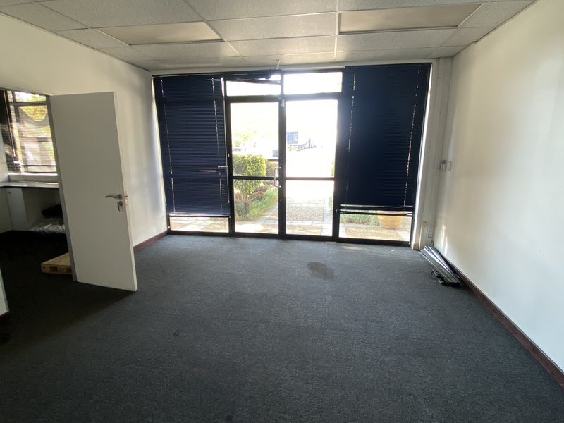 An empty office space featuring carpeted flooring, a suspended ceiling, and a glass entrance door with integrated blinds.