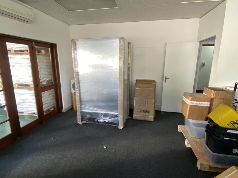 A functional office space featuring carpet flooring, a suspended ceiling, and timber-framed glass doors providing natural light and access.