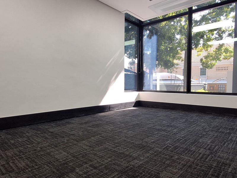 A bright, empty office space featuring large floor-to-ceiling windows, dark carpet flooring, and modern black trim finishes.