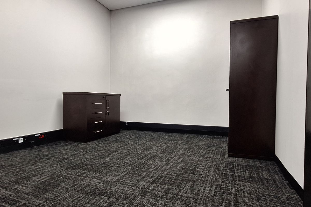 A clean, empty office space featuring dark carpet flooring, white walls, and integrated electrical outlets, suitable for a professional workspace.