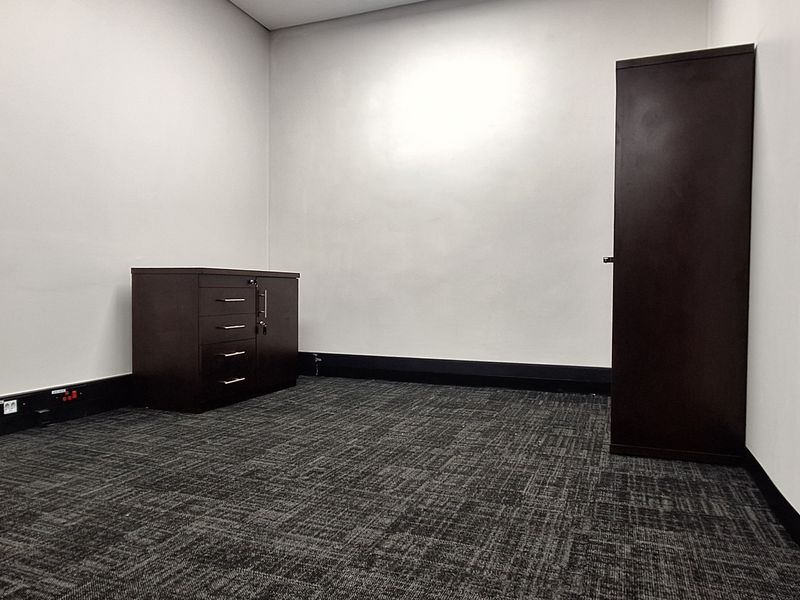 A clean, empty office space featuring dark carpet flooring, white walls, and integrated electrical outlets, suitable for a professional workspace.