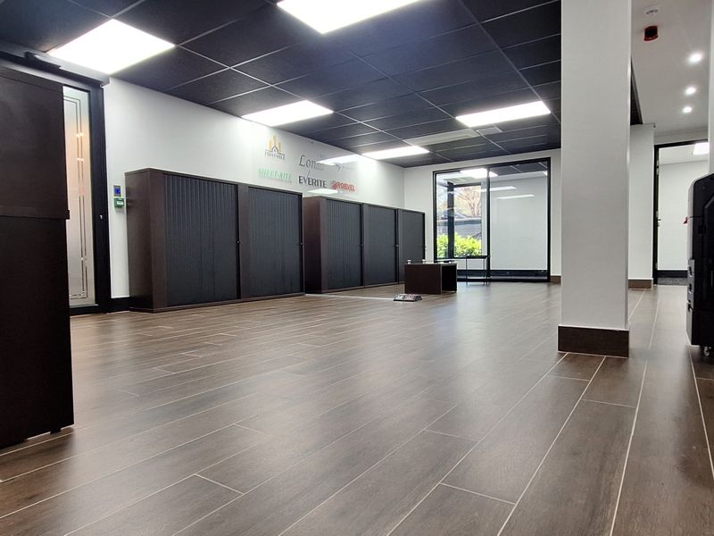 Modern open-plan office space featuring dark wood-look flooring, a black suspended ceiling with recessed lighting, and integrated storage cabinetry.