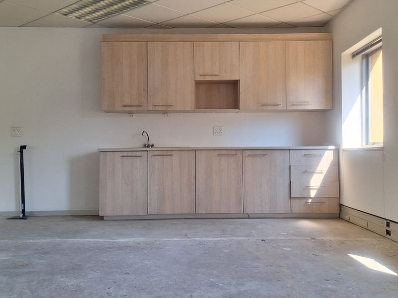 An empty office kitchenette featuring light wood-finish cabinetry, a sink, and a suspended ceiling, ready for flooring installation and final fit-out.