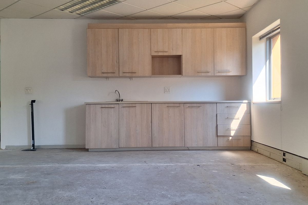 An empty office kitchenette featuring light wood-finish cabinetry, a sink, and a suspended ceiling, ready for flooring installation and final fit-out.