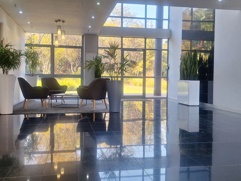 A bright and modern office building entrance lobby featuring polished dark floor tiles, expansive floor-to-ceiling windows, and a clean, professional aesthetic.