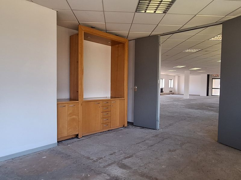 An empty office space featuring a suspended ceiling, recessed lighting, and built-in wooden cabinetry, with an open-plan area visible through double doors.